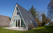 Maison de vacances en A en Allemagne avec terrasse, chaises extérieures et pelouse sous ciel bleu.