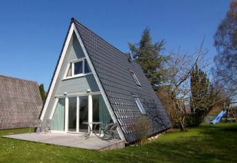 A-frame holiday home in Germany with patio, outdoor chairs, and a garden lawn under clear blue sky.