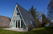 Casa de vacaciones tipo A en Alemania con terraza, sillas exteriores y césped bajo un cielo azul.