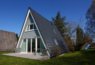 Maison de vacances en A en Allemagne avec terrasse, chaises extérieures et pelouse sous ciel bleu.