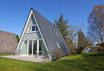 A-vormig vakantiehuis met terras en tuin onder een blauwe lucht, gelegen in Duitsland.