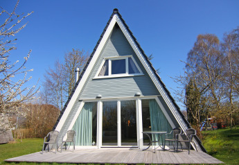 A-frame lodge with patio, outdoor chairs, and large windows at Holiday home Damp, Germany, viewed frontally.