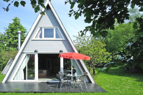A-vormige lodge met grote ramen, terras en rode parasol in groene tuin, Holiday Home Damp, Duitsland.