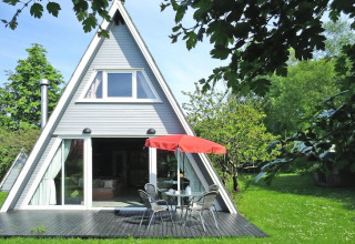 A-vormige lodge met grote ramen, terras en rode parasol in groene tuin, Holiday Home Damp, Duitsland.