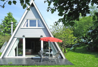 Casa vacacional tipo cabaña A con fachada acristalada, terraza y sombrilla roja en Damp, Alemania.