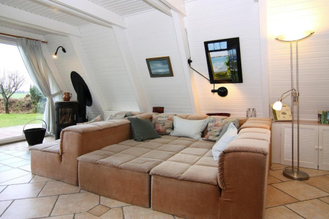 Sala de estar con gran sofá beige, paredes claras y vistas al jardín en la casa de vacaciones Damp, Alemania.