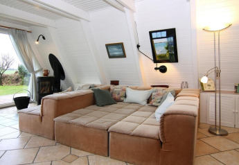 Stue med stor beige sofa, lyse vægge og vinduer i ferieboligen Damp, Tyskland, med udsigt til haven.