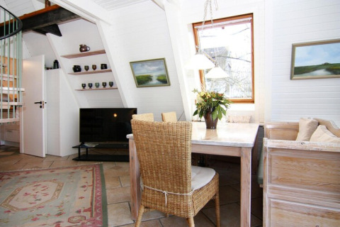 Lichte zithoek in vakantiehuis Damp met eettafel, rieten stoel, tv en groot raam in Duitsland.