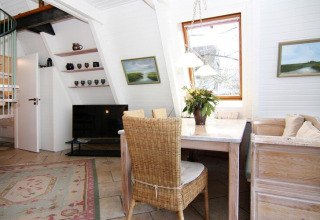 Sala luminosa del Holiday home Damp con mesa de comedor, silla de mimbre, TV y ventana grande en Alemania.