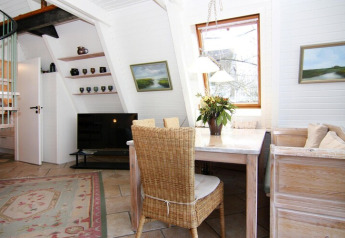 Lichte zithoek in vakantiehuis Damp met eettafel, rieten stoel, tv en groot raam in Duitsland.