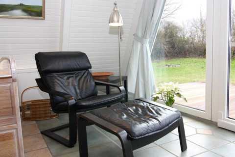 Sillón cómodo con reposapiés junto a la ventana en casa de vacaciones, vista al jardín y decoración moderna.