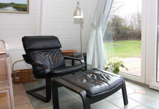 Comfortabele zetel met voetenbank bij raam in vakantiewoning, uitzicht op tuin en moderne inrichting.