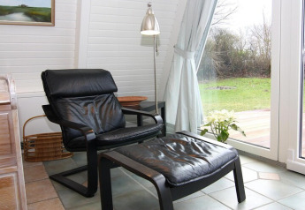 Fauteuil confortable avec repose-pieds près de la fenêtre d'une maison de vacances, vue sur jardin moderne.