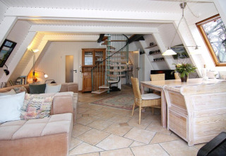 Salón luminoso con escalera de caracol, sofá de esquina y mesa de comedor en la casa de vacaciones Damp.