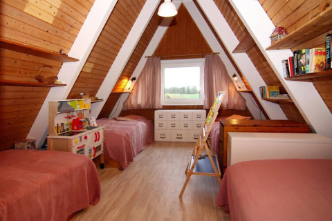 Children’s room in an A-frame wooden lodge with three beds, shelves, toys, books, and a large window.