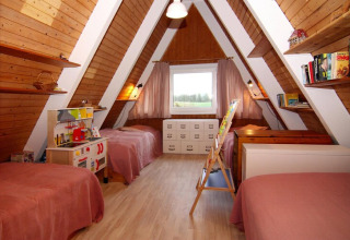 Dormitorio infantil en cabaña A-frame de madera con tres camas, estanterías, juguetes y ventana grande.