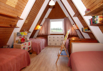 Kinderkamer in een A-frame houten lodge met drie bedden, speelgoedkeuken, boeken en groot raam.