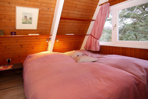 Chambre avec murs en bois, lit double avec draps roses, grande fenêtre donnant sur la forêt, Holiday home Damp.
