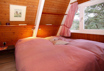Dormitorio con paredes de madera, cama doble con ropa rosa y ventana grande con vista al bosque en Holiday home Damp.