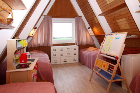 Gezellige kinderkamer met twee eenpersoonsbedden, speelgoedkeuken en bord in een A-frame houten lodge.