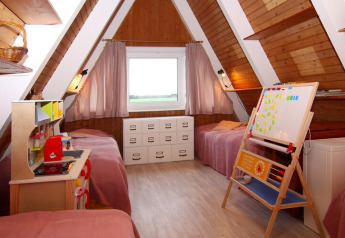 Gezellige kinderkamer met twee eenpersoonsbedden, speelgoedkeuken en bord in een A-frame houten lodge.