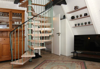 Living room in a holiday home featuring a spiral staircase, wooden cabinet, TV, and shelves with pottery.