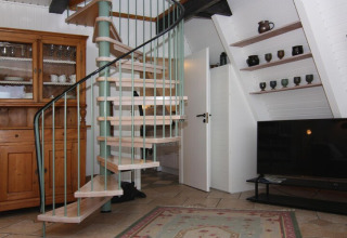 Sala de estar en casa de vacaciones con escalera de caracol, mueble de madera, TV y estantes con cerámica.