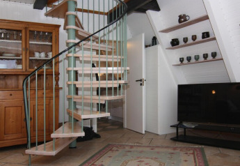 Living room in a holiday home featuring a spiral staircase, wooden cabinet, TV, and shelves with pottery.