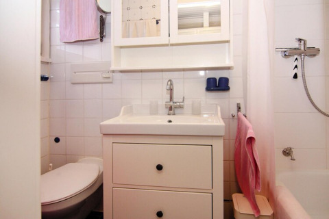 Helles, kompaktes Badezimmer mit weißem Interieur, Waschbecken, Toilette, Spiegel und rosa Handtüchern.