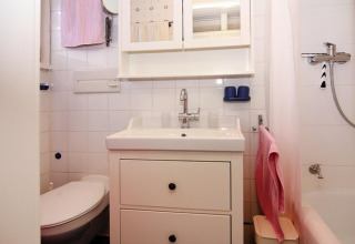 Lichte, compacte badkamer met een witte wastafel, toilet, spiegelkast, douche en roze handdoeken.