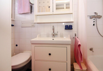 Petite salle de bain lumineuse avec carrelage blanc, lavabo, armoire à miroir, douche et serviettes roses.