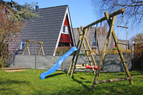 Parco giochi con altalene e scivolo davanti a una casa vacanze a forma di A in Germania in una giornata serena.