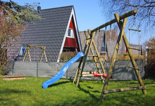 Speeltuin met schommel en glijbaan naast een A-vormig vakantiehuis in Duitsland op een mooie dag.