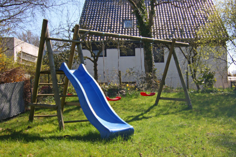 Speelplek met glijbaan en schommels in de tuin van Holiday home «Damp 90 sqm 5 Persons» in Duitsland.