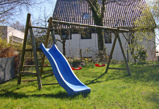 Playground with slide and swings in the garden of Holiday home «Damp 90 sqm 5 Persons» in Germany.