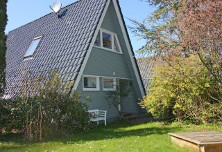 A-frame house with a dark tiled roof and garden greenery at Holiday home «Damp 90 sqm 5 Persons» in Germany.