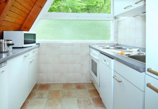 Lichte, compacte keuken met schuin plafond, witte kasten en groot raam met uitzicht op bomen in Duitsland.