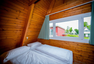 Cozy wooden lodge bedroom with double bed and wide window overlooking other colorful lodges outside.