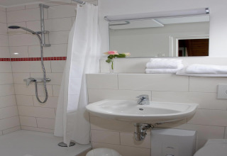 Modern lodge bathroom featuring a shower, sink, mirror, stacked towels, and a single rose in a vase.