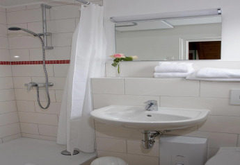 Modern lodge bathroom featuring a shower, sink, mirror, stacked towels, and a single rose in a vase.