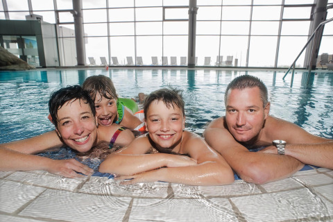 Family of four enjoys spending time together in an indoor lodge swimming pool with large windows.