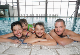 Family of four enjoys spending time together in an indoor lodge swimming pool with large windows.