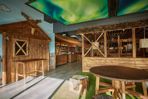 Interno di lodge moderno con mobili in legno rustici, area bar e soffitto con effetto aurora boreale.