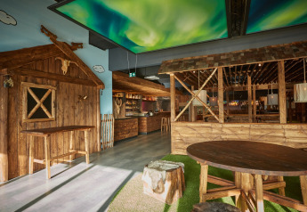 Modern lodge interior with rustic wooden furniture, bar area, and a ceiling featuring northern lights design.