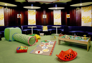 Speelruimte voor kinderen in een lodge met tunnel, speelmat, blokken en gezellige zithoeken eromheen.