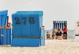 Gezin geniet van een zonnige dag op het strand, zittend in blauwe gestreepte strandstoelen aan zee.