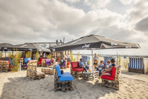 Strandlounge aan Nurdachhaus HiPr met palletmeubels, parasols en genietende gasten in Duitsland.