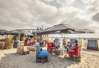 Outdoor beach lounge at Nurdachhaus HiPr with pallet furniture, umbrellas, and guests relaxing in Germany.