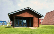 Chalet en bois avec terrasse couverte et mobilier de jardin, entouré d’herbe et d’autres maisons colorées.
