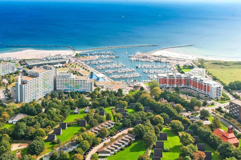Veduta aerea di un porto turistico con barche, hotel, aree verdi e bungalow vicino al mare in una giornata limpida.
